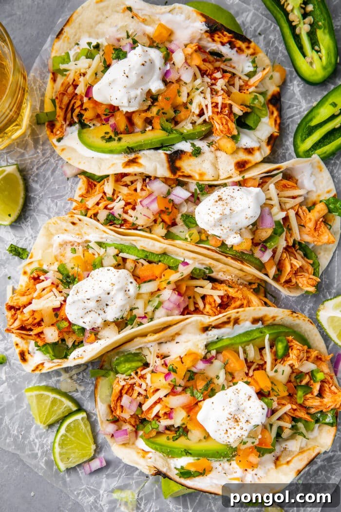 Four shredded chicken tacos arranged on a sheet of parchment paper, showcasing their vibrant toppings.