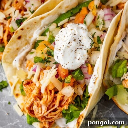 Close up of a shredded chicken taco with sour cream, highlighting the rich filling and fresh toppings.
