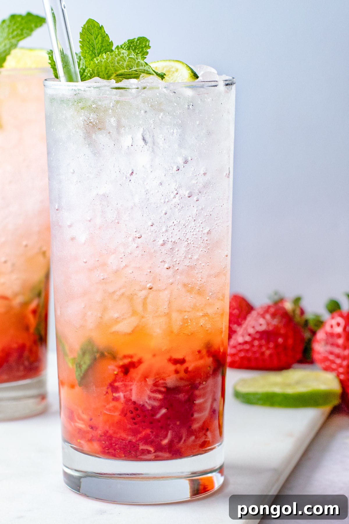 Ruby Mint Breeze 2 A tall highball glass containing a strawberry mojito, with rum and ice layer on top of muddled strawberries and mint.