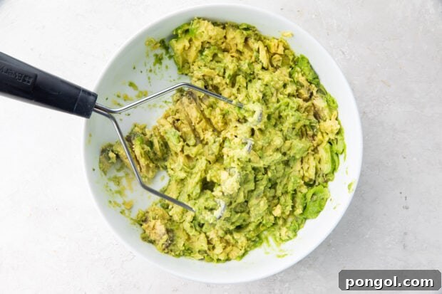 Mashed avocado in bowl with potato masher