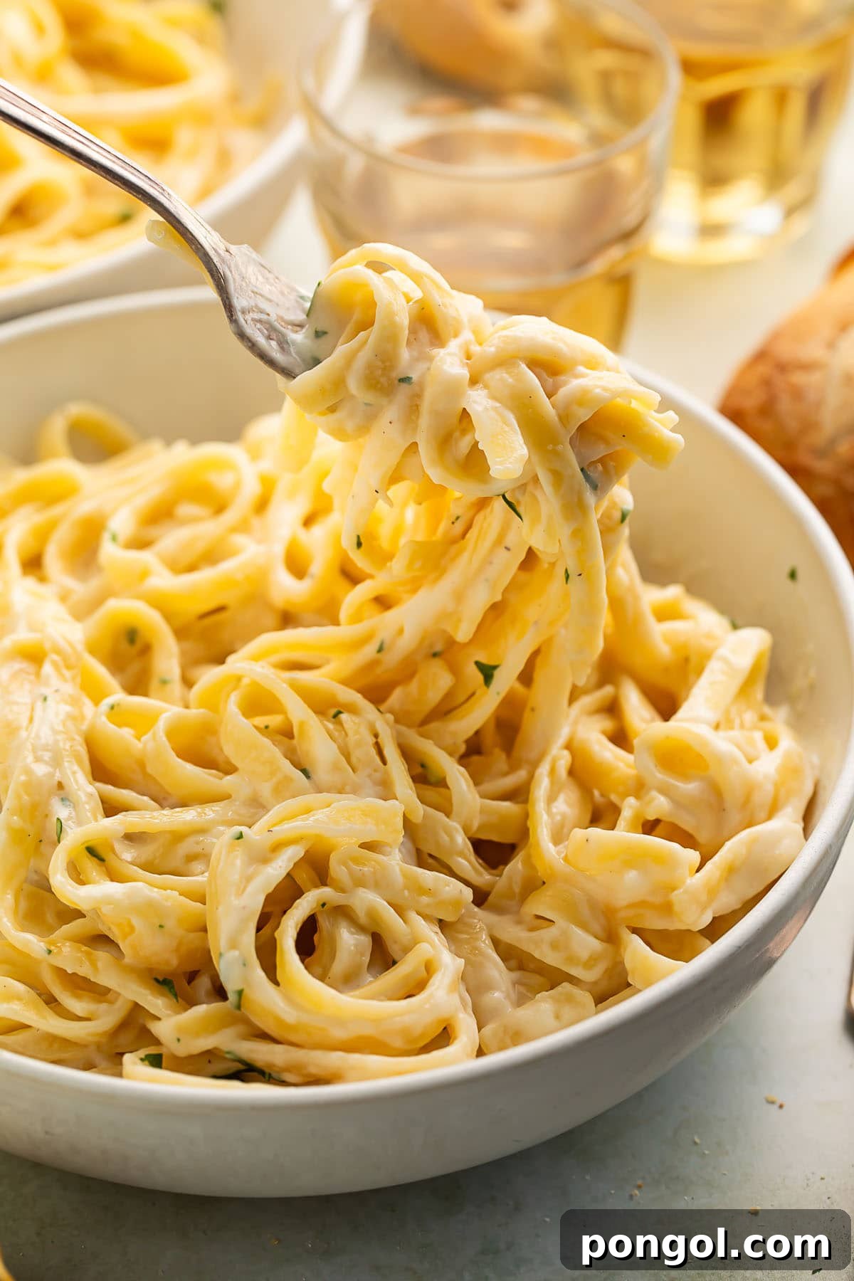 A fork lifts a generous swirl of fettuccine coated in creamy cottage cheese alfredo from a large serving bowl, highlighting the sauce's rich texture.