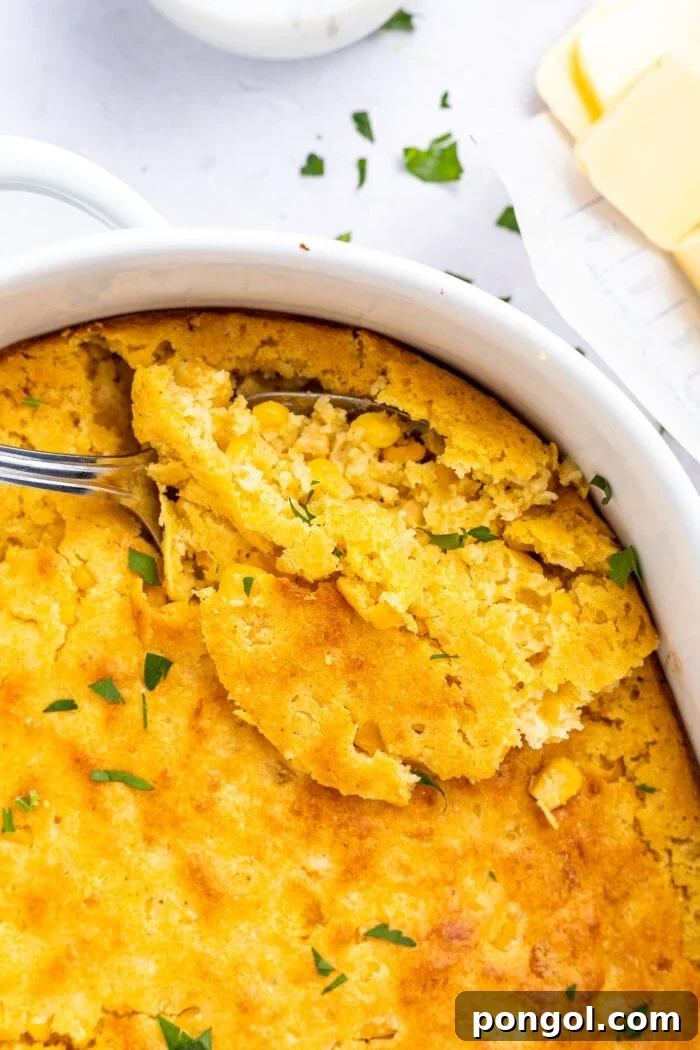 Golden Cornbread Delight 3 Overhead image on cornbread casserole being scooped out of baking dish with sliced butter on the side, showing the soft interior.
