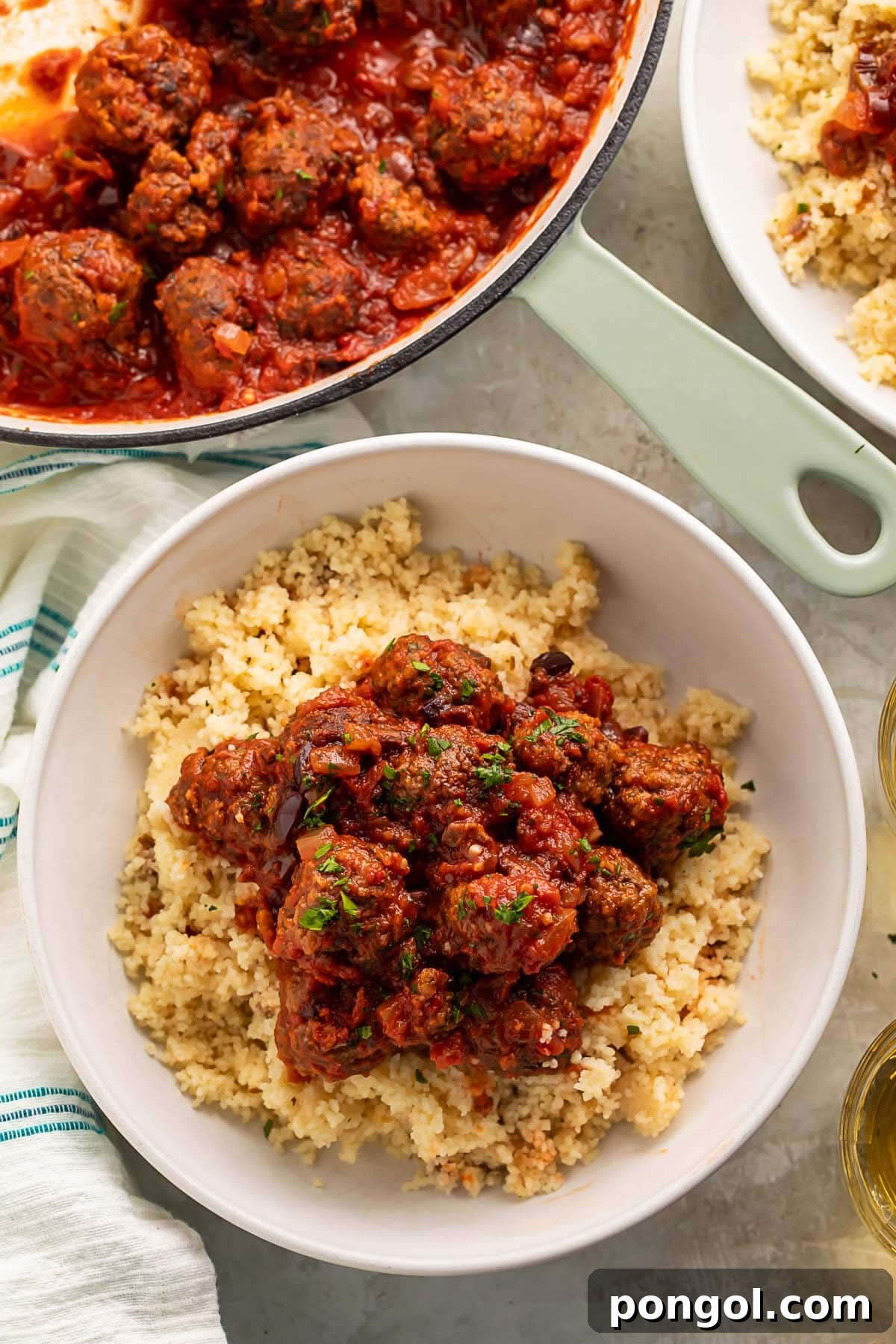 Moroccan meatballs served over a bed of fluffy couscous in a large white bowl.