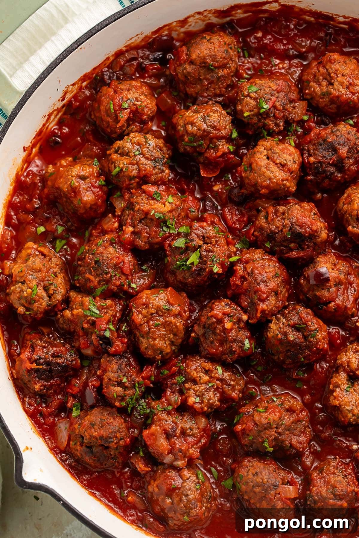 A large pan of Moroccan meatballs in a deep red sauce garnished with fresh herbs.