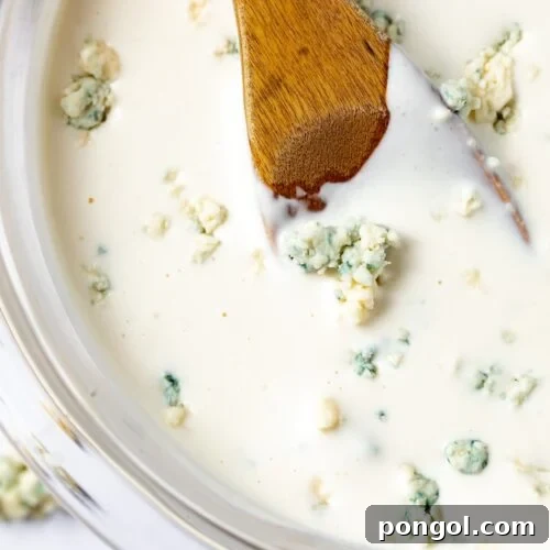 Bold Roquefort Dressing 4 A top-down view of creamy Roquefort dressing in a white bowl with a wooden spoon.