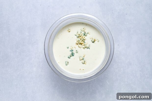 Bold Roquefort Dressing 6 Crumbled Roquefort cheese being gently stirred into the creamy dressing base.