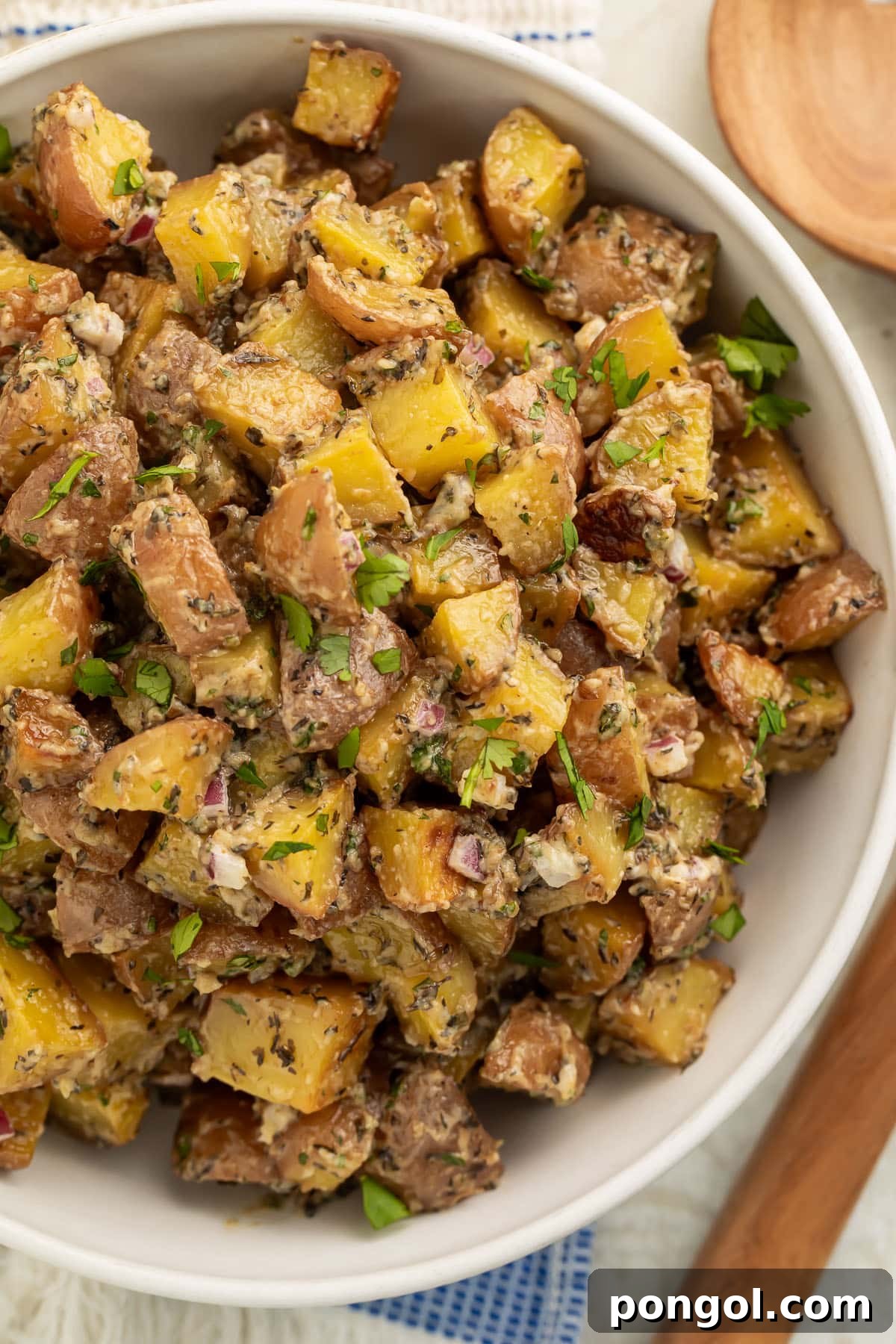 Overhead view of a large bowl of roasted potato salad with diced roasted potatoes, fresh herbs, and red onions.