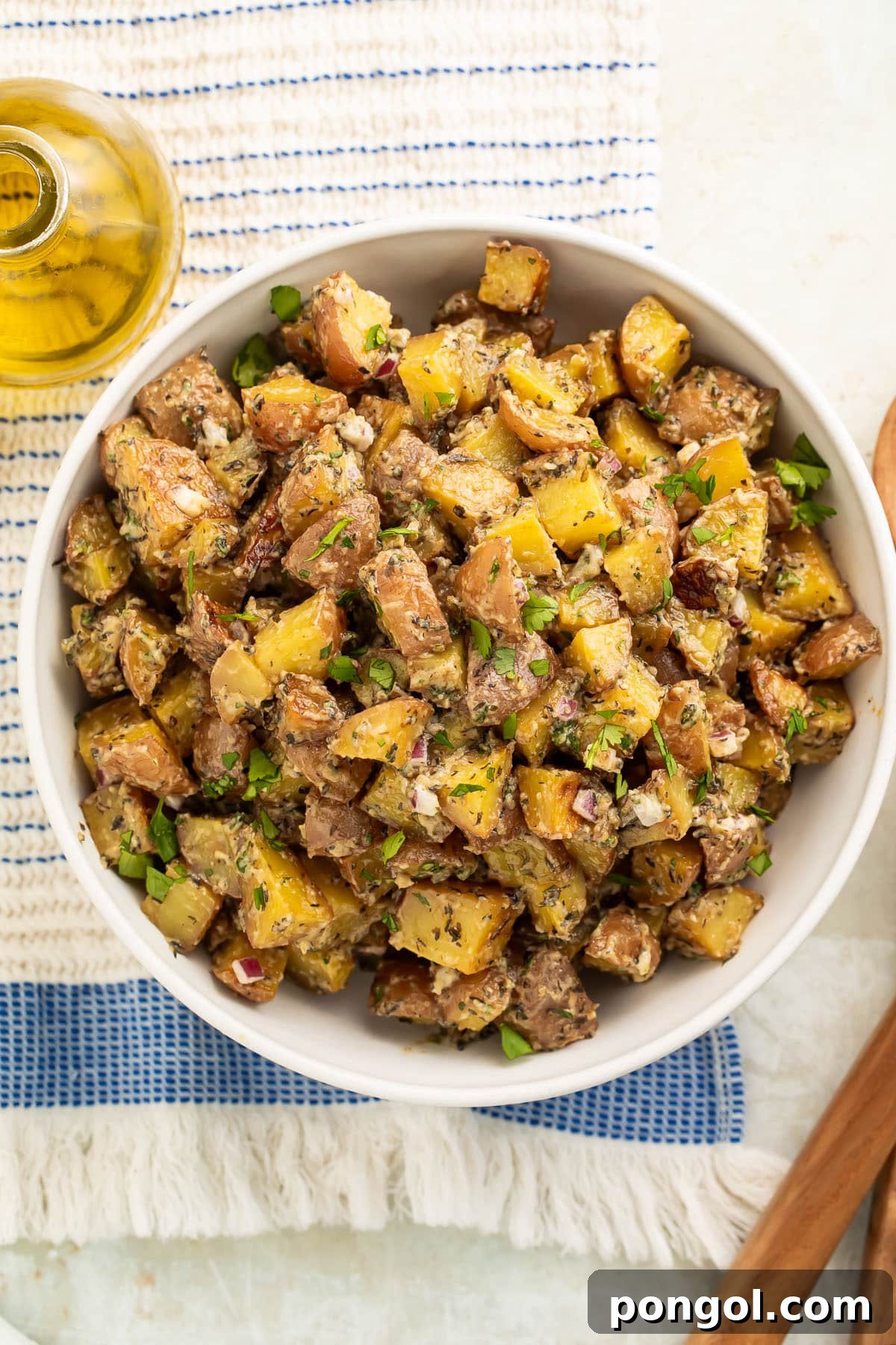 Overhead view of a large bowl of roasted potato salad with diced roasted potatoes, fresh herbs, and red onions.