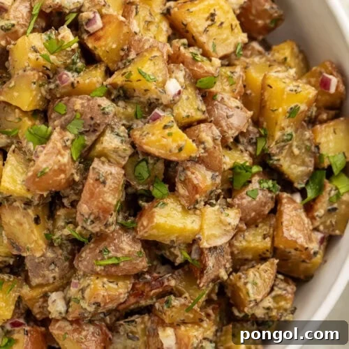 Overhead view of a large bowl of roasted potato salad with diced roasted potatoes, fresh herbs, and red onions.