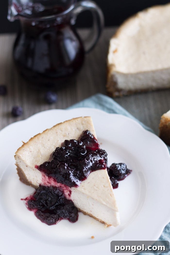 Hand carefully placing a generous spoonful of luscious Blueberry White Wine Sauce onto a Vegan Lemon Ricotta Cheesecake