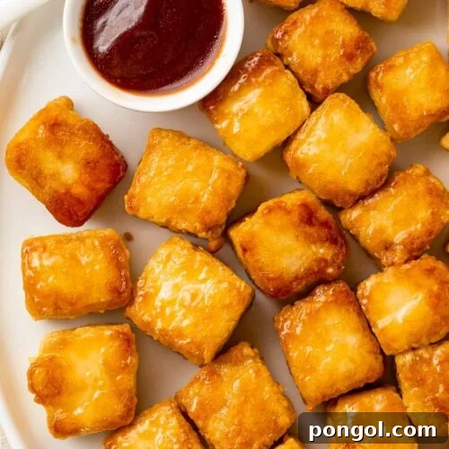 Crispy baked tofu cubes arranged on a plate next to a ramekin of BBQ sauce.