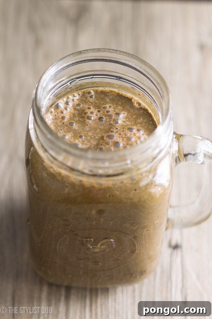 Glass of Brownie Batter Green Smoothie with a spoon, showing a rich, creamy texture.