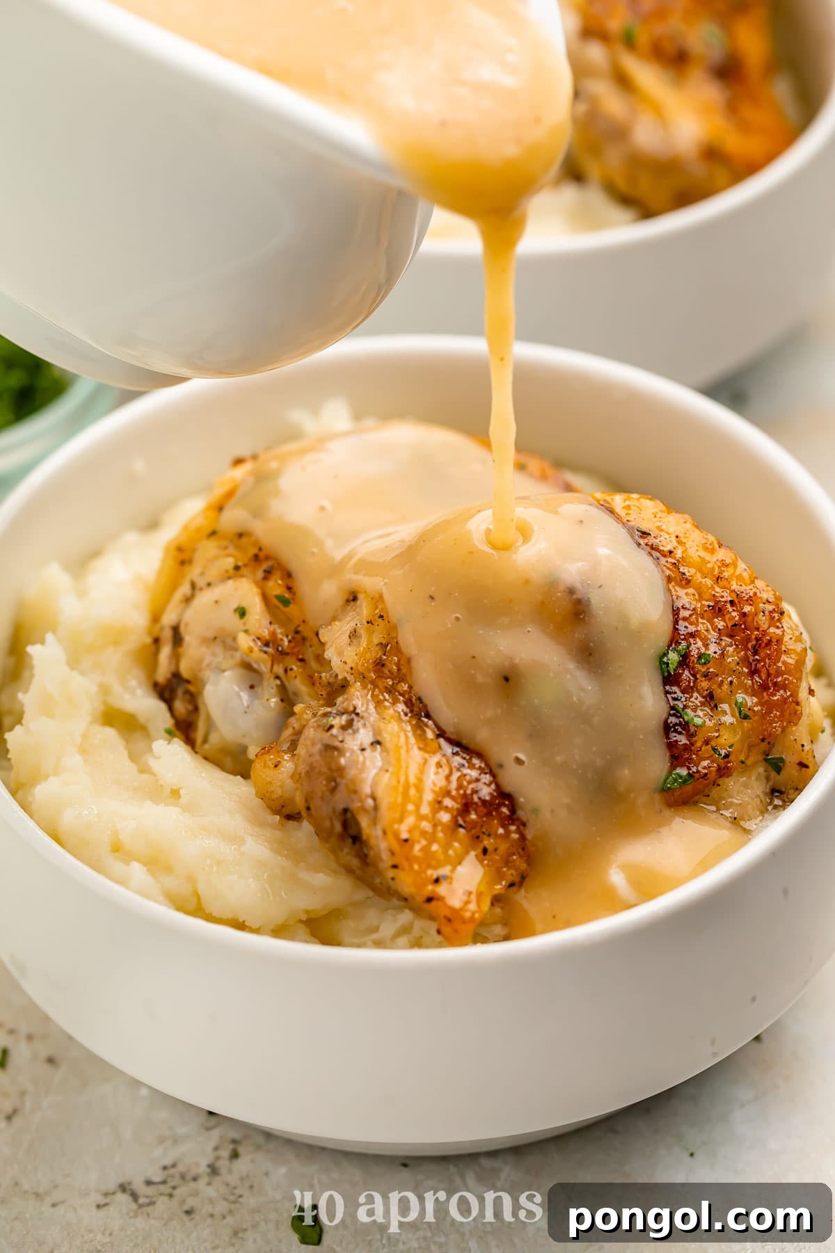 125 Simple Chicken Dinners: Fast Meals with Pantry Staples 11 A chicken thigh, cooked in the Instant Pot, resting on top of mashed potatoes in a white bowl with gravy being poured over the chicken.