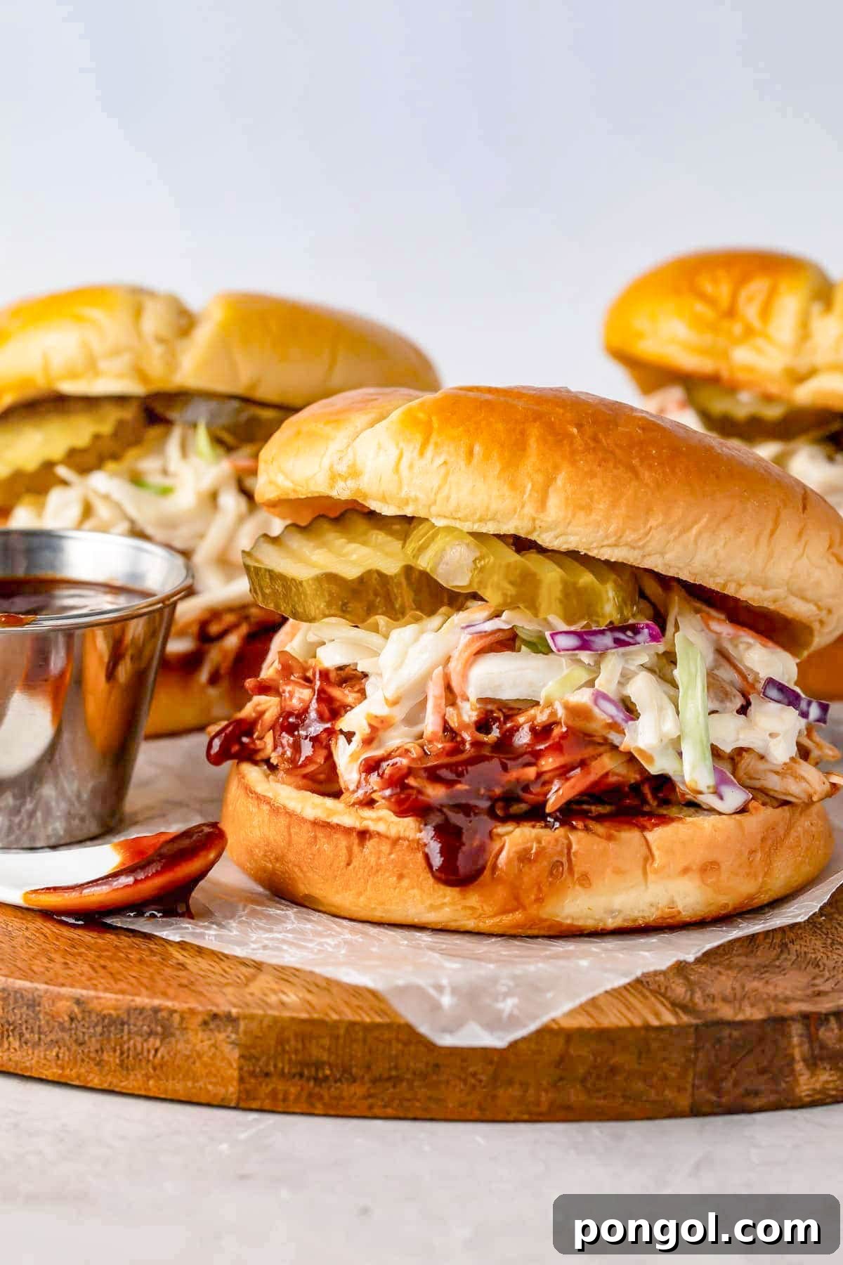 125 Simple Chicken Dinners: Fast Meals with Pantry Staples 102 Instant Pot pulled bbq chicken sandwiched between two hamburger bun halves with coleslaw and pickles.