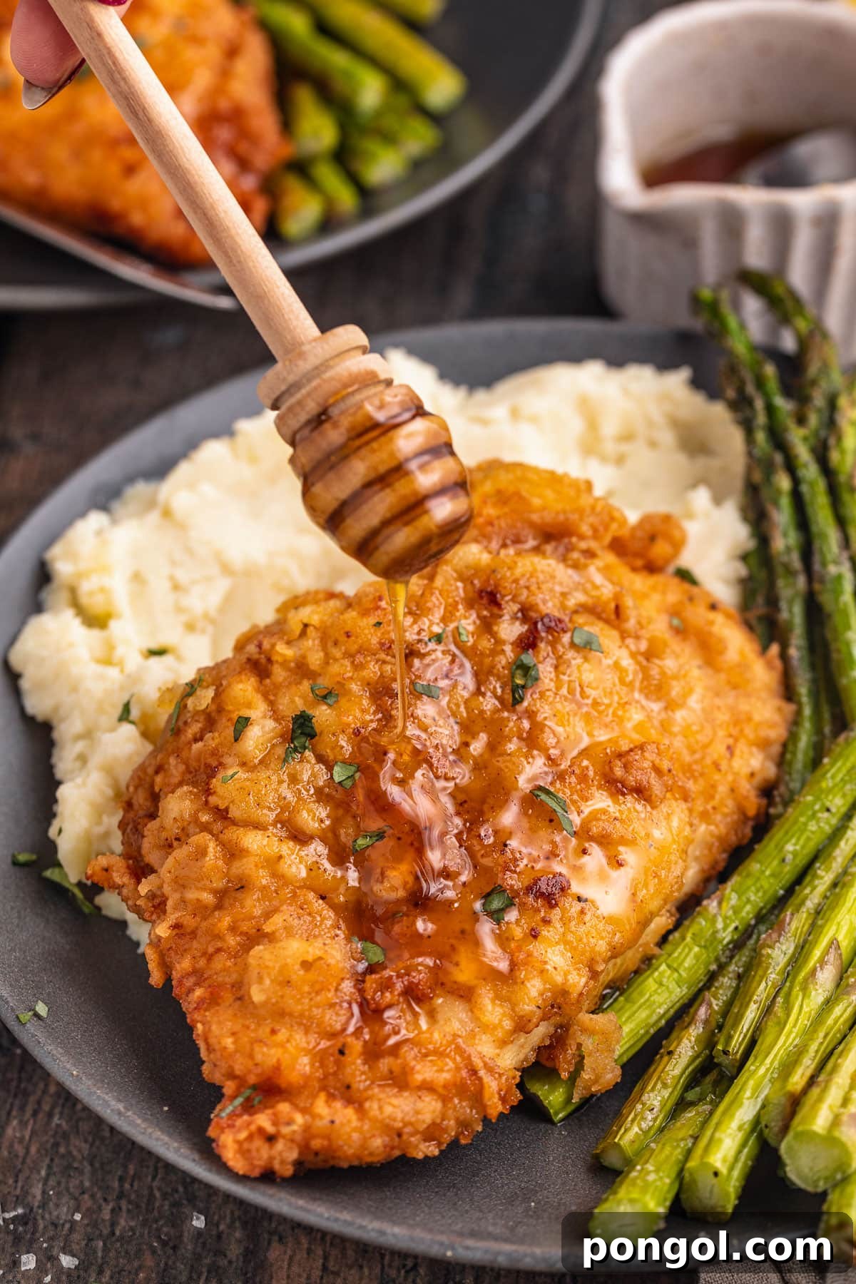 125 Simple Chicken Dinners: Fast Meals with Pantry Staples 113 Crispy breaded chicken breast being drizzled with truffle honey on a plate next to asparagus and mashed potatoes.