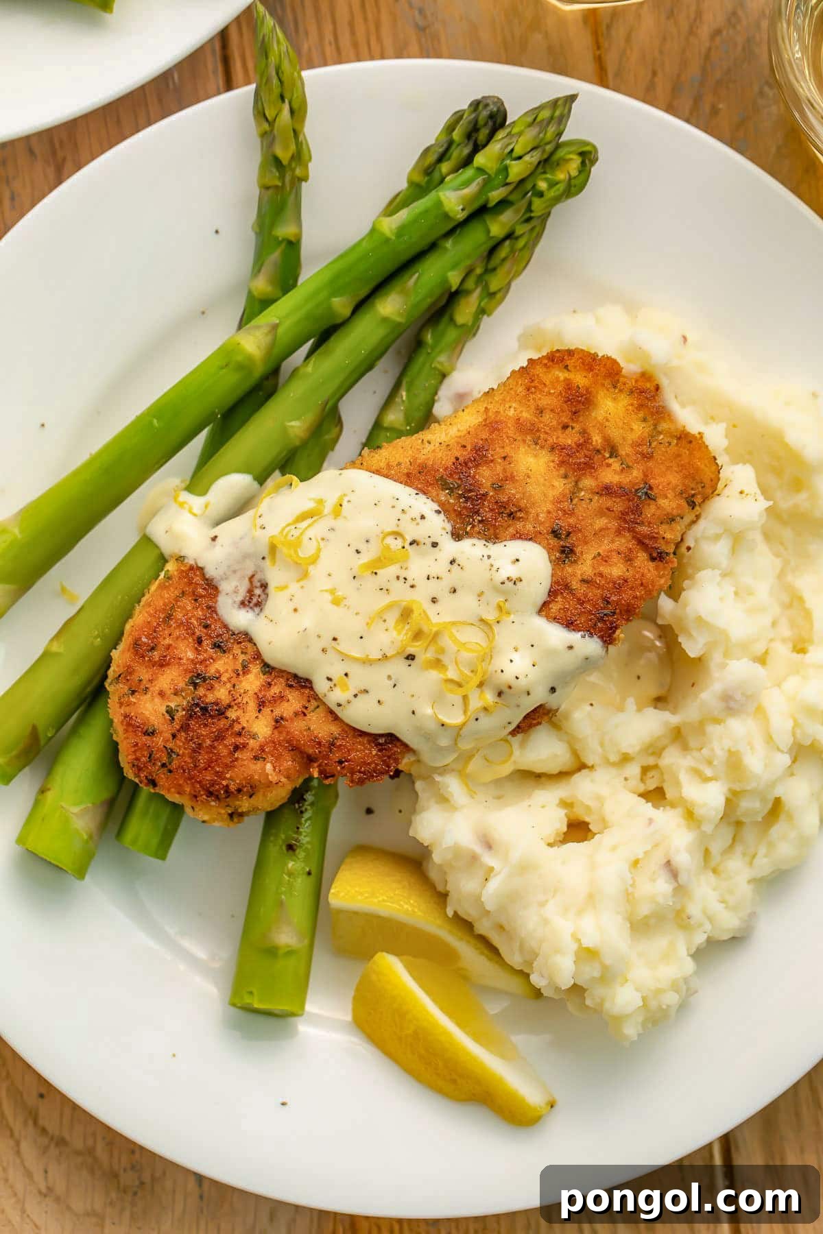 125 Simple Chicken Dinners: Fast Meals with Pantry Staples 122 Copycat chicken costoletta on a white plate with mashed potatoes, green asparagus, and a creamy sauce.