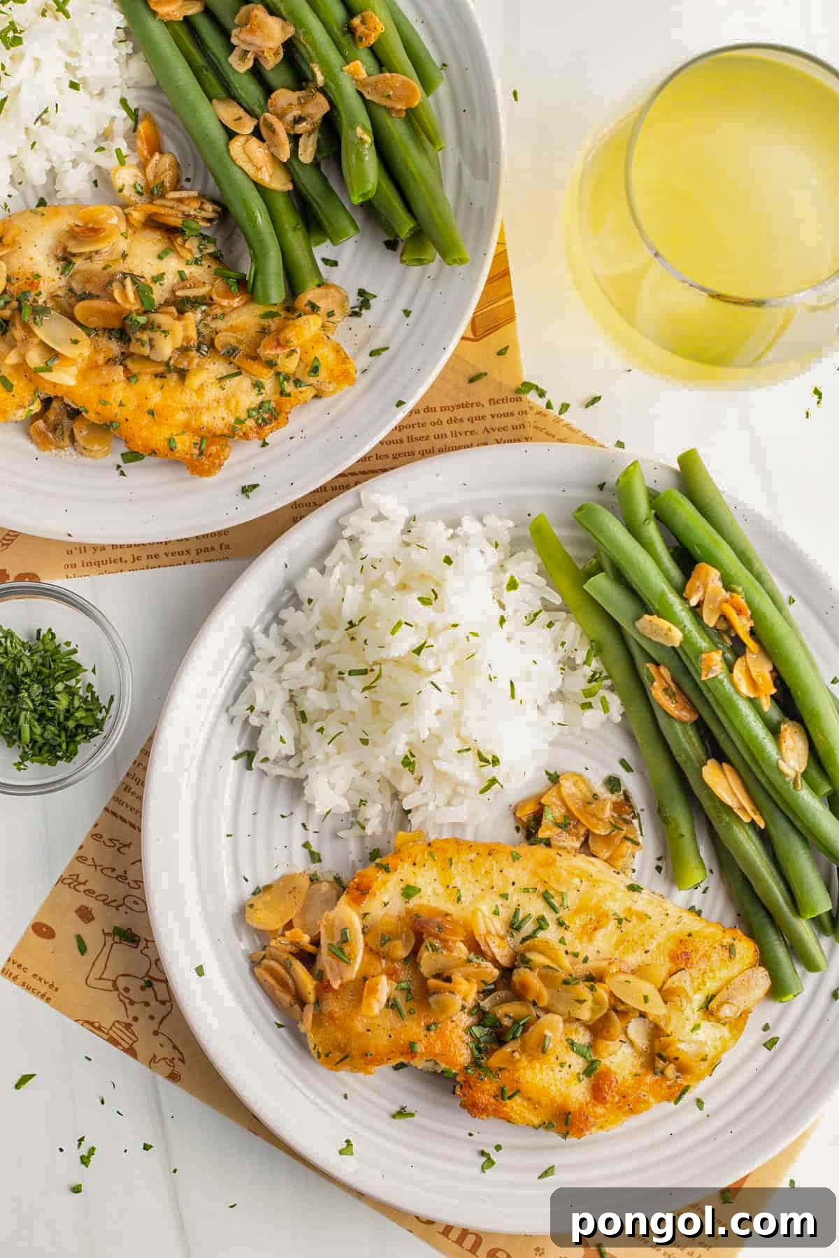 125 Simple Chicken Dinners: Fast Meals with Pantry Staples 127 Chicken almondine on a white plate with white rice, green asparagus, almond slivers, next to a glass of white wine.