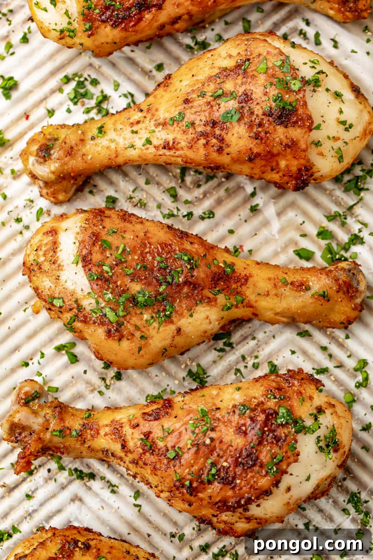 125 Simple Chicken Dinners: Fast Meals with Pantry Staples 27 Top-down photo of seasoned air fryer chicken legs on a baking sheet with fresh herbs.