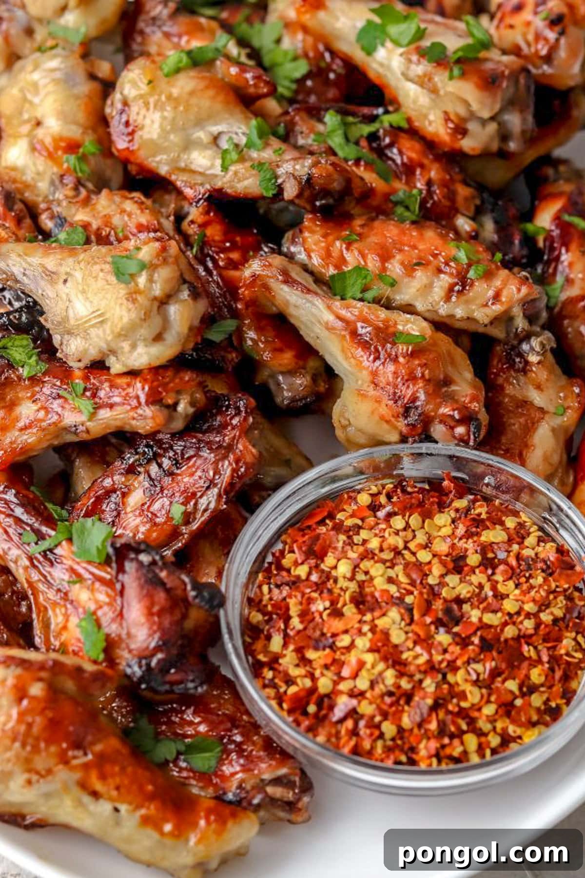 125 Simple Chicken Dinners: Fast Meals with Pantry Staples 34 Juicy brined and cooked chicken wings piled on a platter next to a glass serving bowl of sauce with red pepper flakes.
