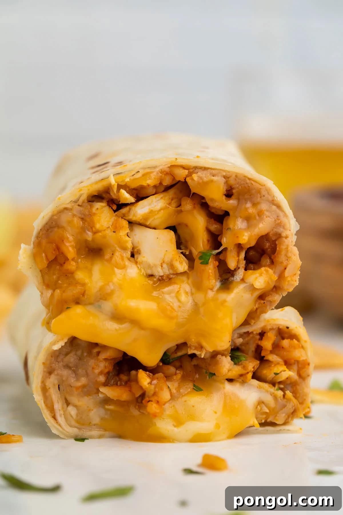 125 Simple Chicken Dinners: Fast Meals with Pantry Staples 37 Two halves of a bean and chicken burrito with melted cheese, stacked on top of each other to show the filling inside.