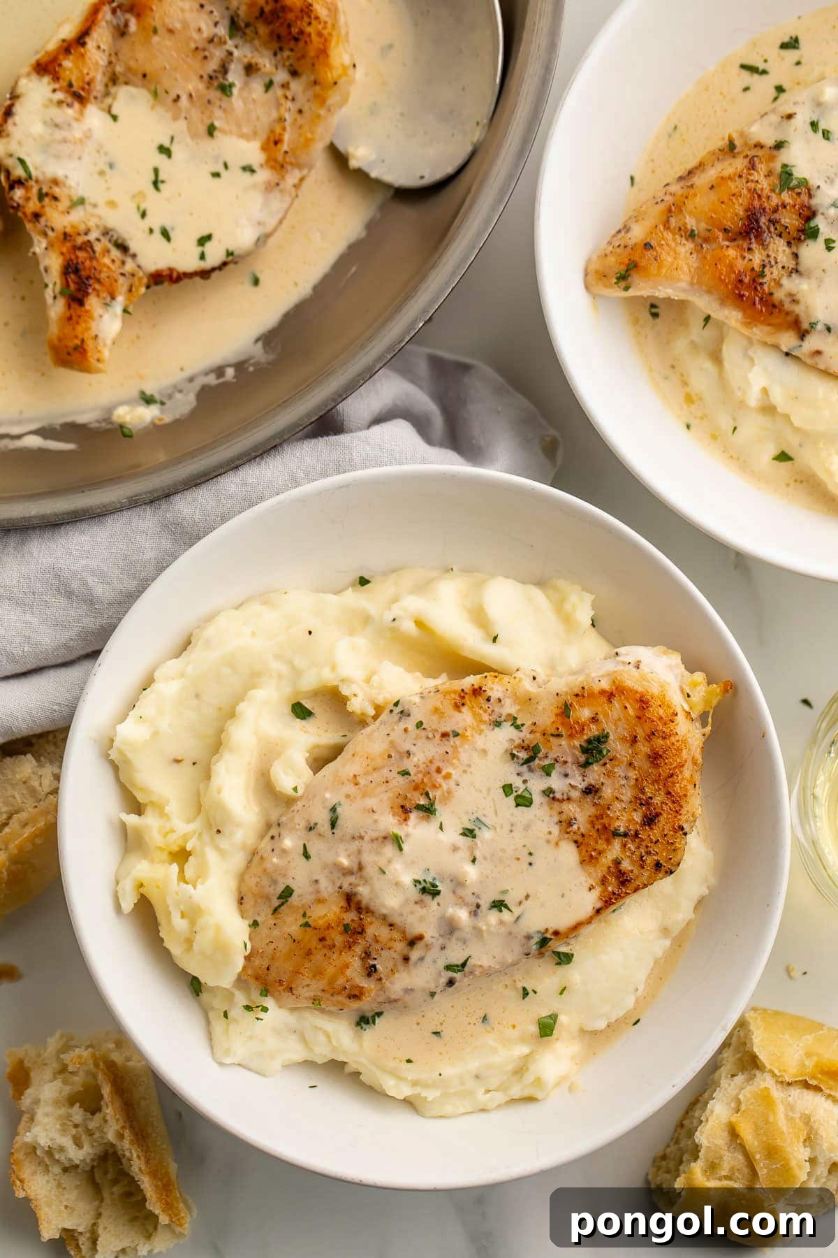 125 Simple Chicken Dinners: Fast Meals with Pantry Staples 39 Top-down look at two bowls of mashed potatoes topped with cream cheese garlic skillet chicken and creamy sauce next to a large skillet.