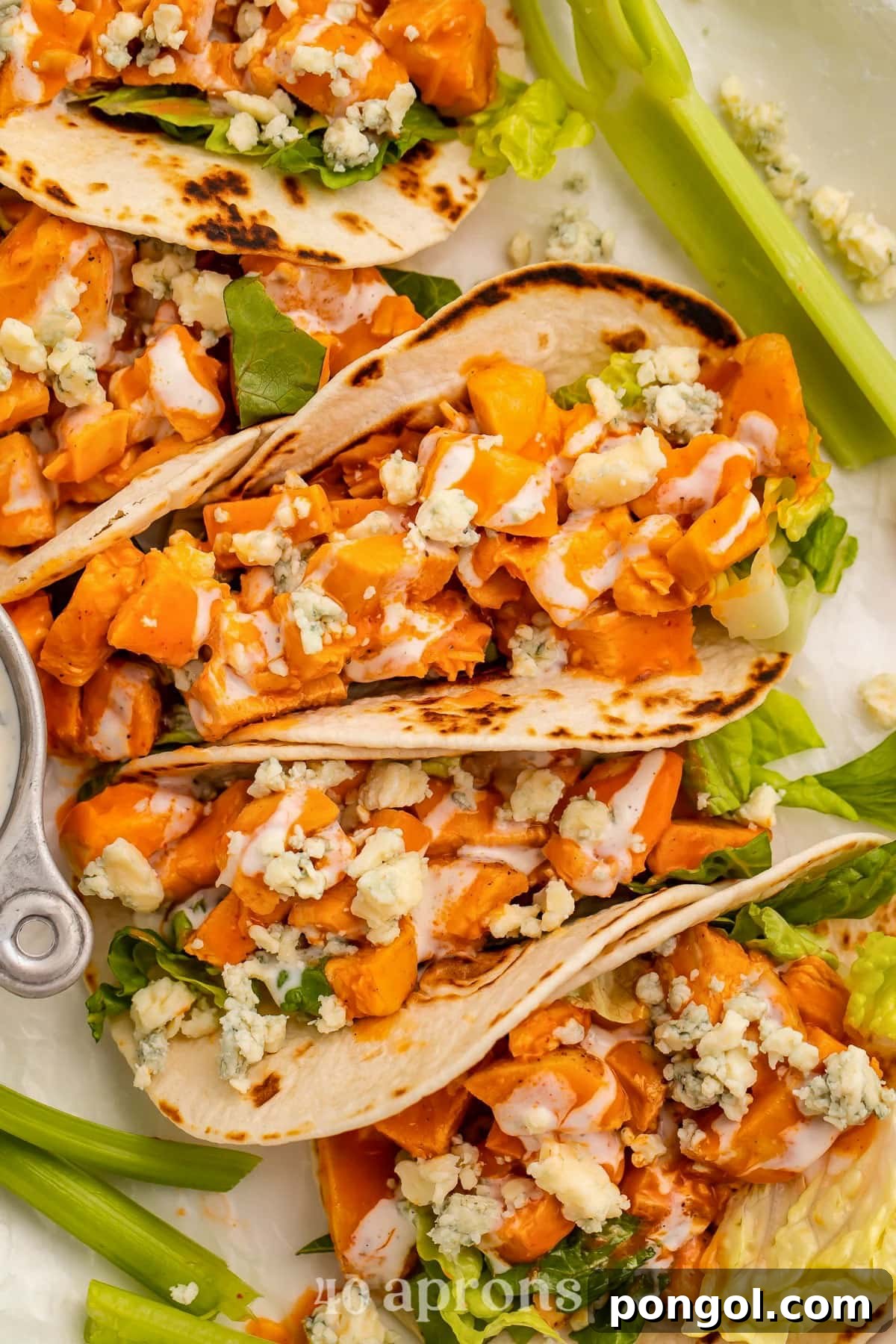 125 Simple Chicken Dinners: Fast Meals with Pantry Staples 47 Top-down look at buffalo chicken in flour tortillas with crumbled cheese lined up on a platter with celery sticks.
