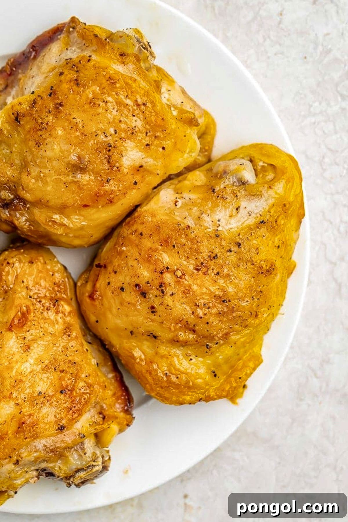 125 Simple Chicken Dinners: Fast Meals with Pantry Staples 7 Previously-frozen chicken thighs, seasoned and then cooked in the Instant Pot, placed on a small white plate on a neutral tabletop.