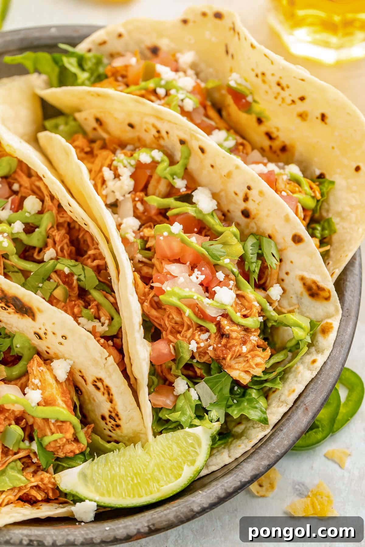 125 Simple Chicken Dinners: Fast Meals with Pantry Staples 68 Close-up of Instant Pot chicken tacos with flour tortillas, lettuce, crumbled queso, pico, and a lime wedge.