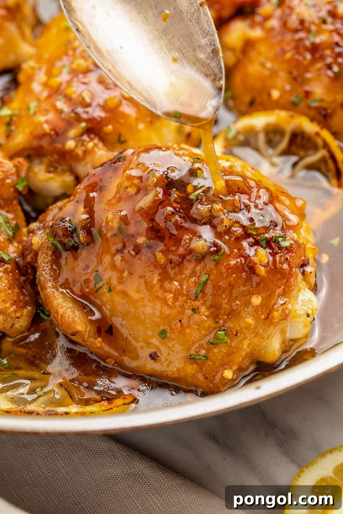125 Simple Chicken Dinners: Fast Meals with Pantry Staples 70 A spoon drizzling a shiny honey garlic glaze over the top of a lemon pepper seasoned chicken thigh.