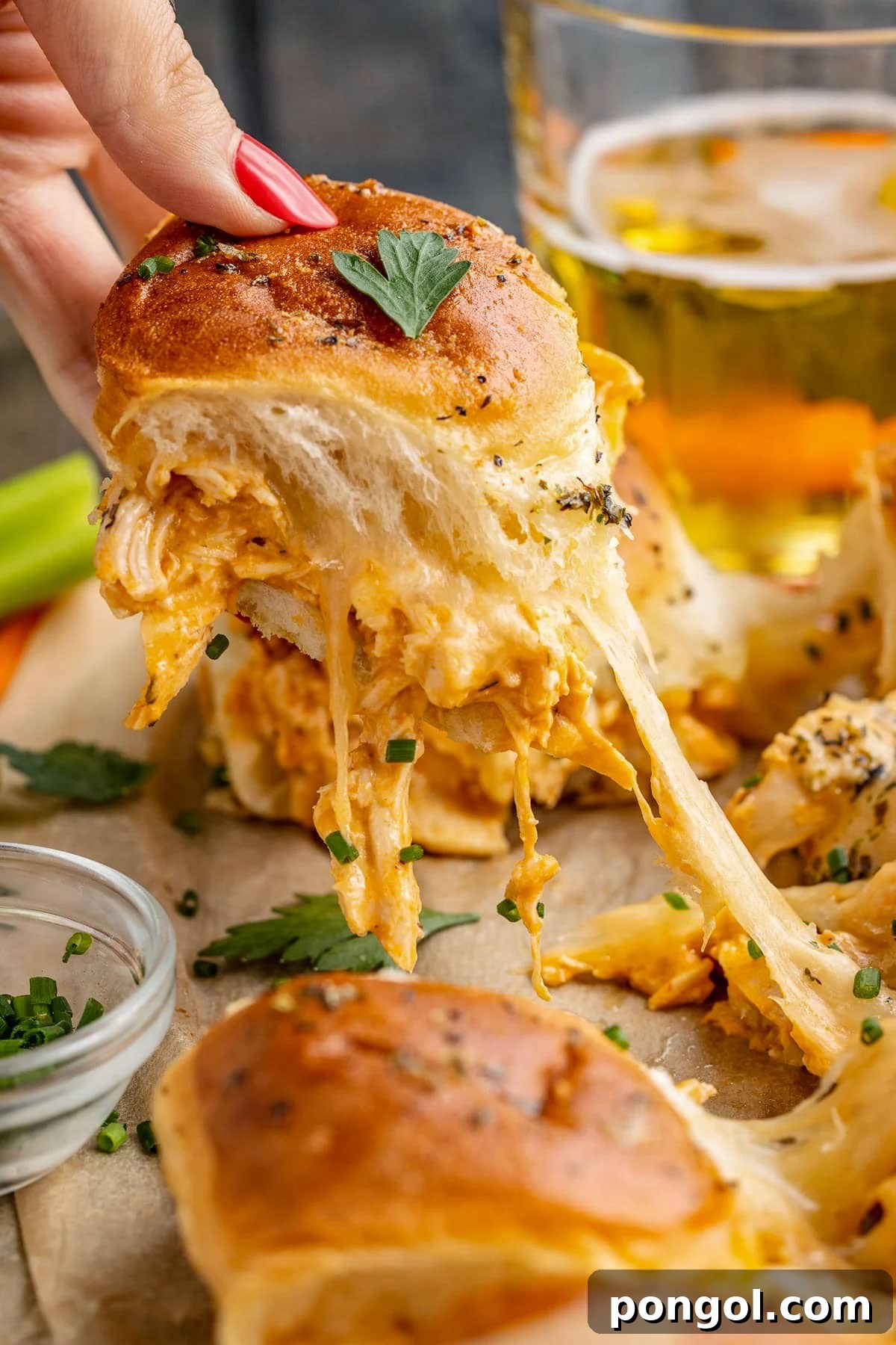 125 Simple Chicken Dinners: Fast Meals with Pantry Staples 79 A white woman's hand pulling a buffalo chicken slider away from a sheet pan, with a long pull of melty cheese connecting the sandwiches.
