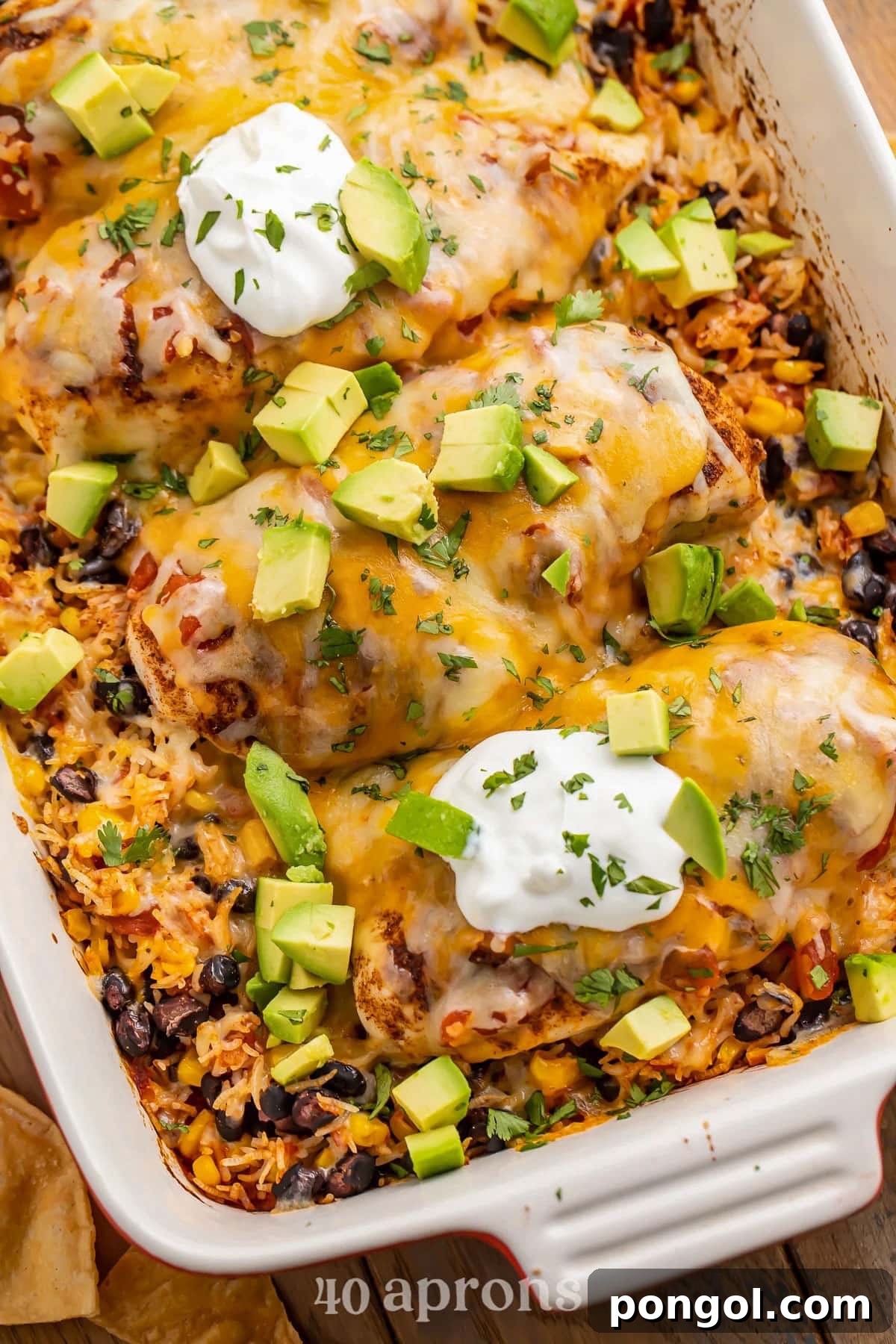 125 Simple Chicken Dinners: Fast Meals with Pantry Staples 84 A casserole dish holding Mexican chicken casserole with rice, beans, and veggies, topped with avocado and sour cream.