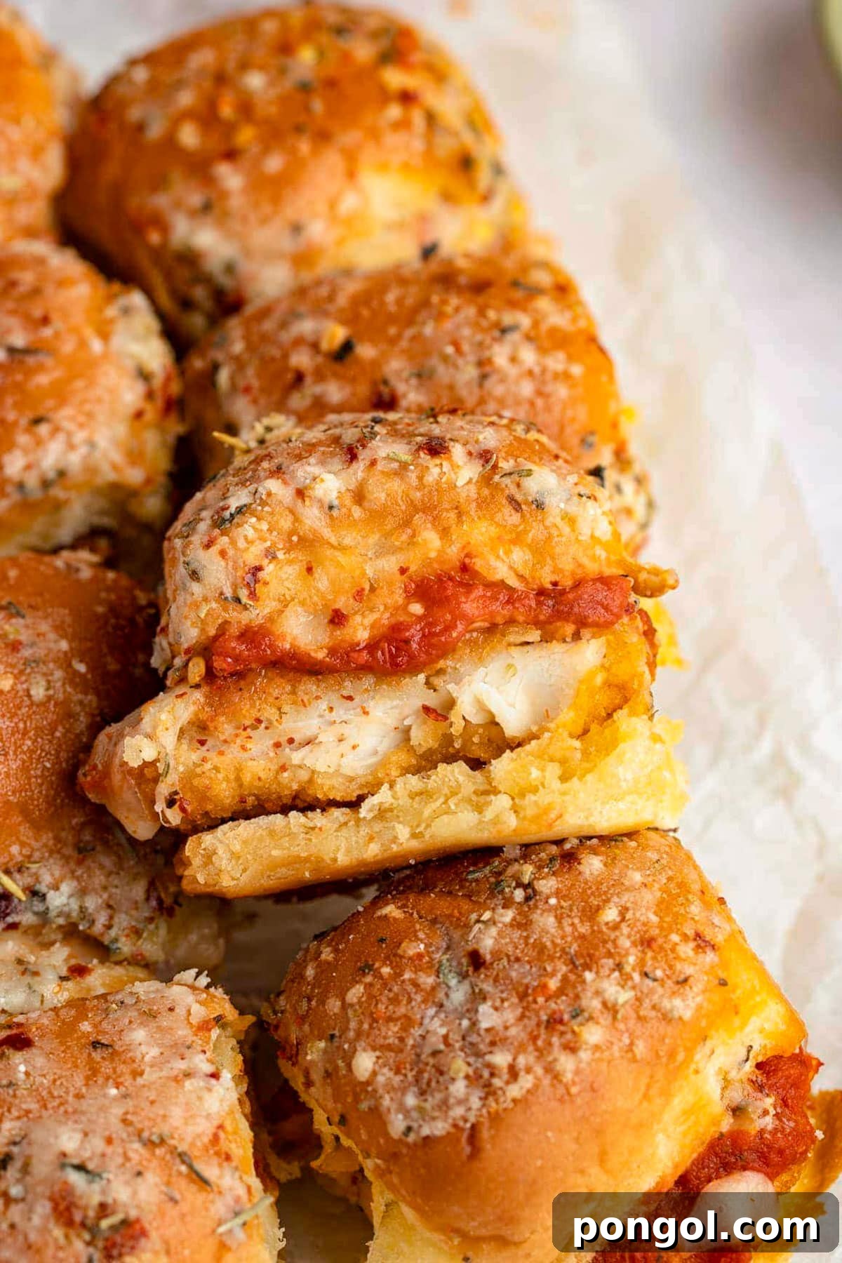 125 Simple Chicken Dinners: Fast Meals with Pantry Staples 91 A tray of crispy chicken parm sliders, with one slider propped up on top of another to show the chicken inside.