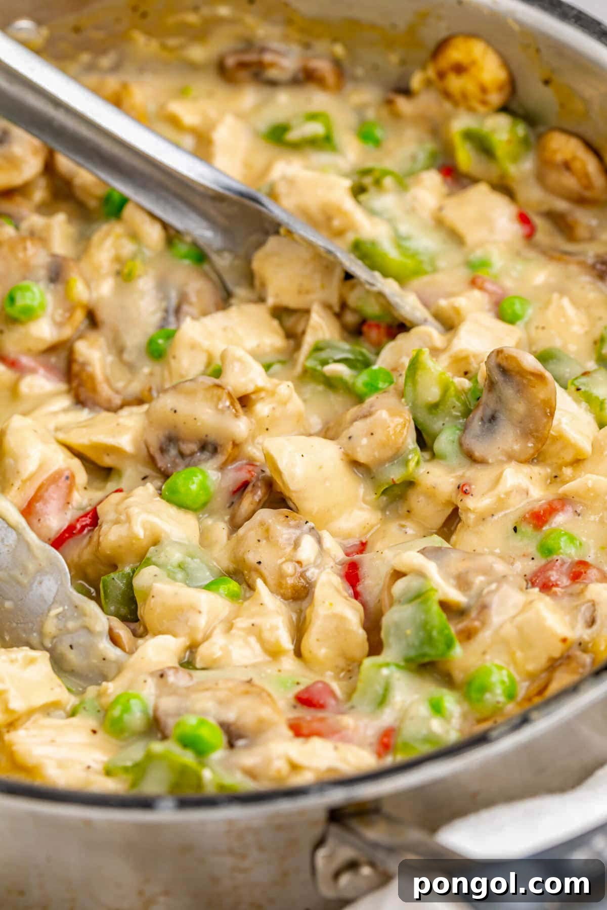 125 Simple Chicken Dinners: Fast Meals with Pantry Staples 94 Creamy chicken a la king in a large silver skillet with bright green peas and a pair of silver tongs.