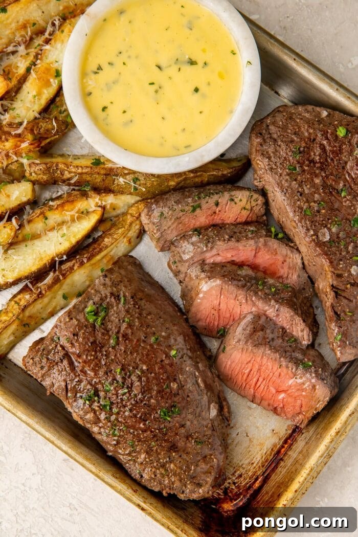 Medium rare steak and thick cut fries with a bowl of bearnaise sauce on a sheet pan