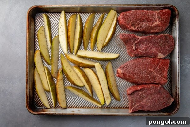 Uncooked steak and fries on baking sheet