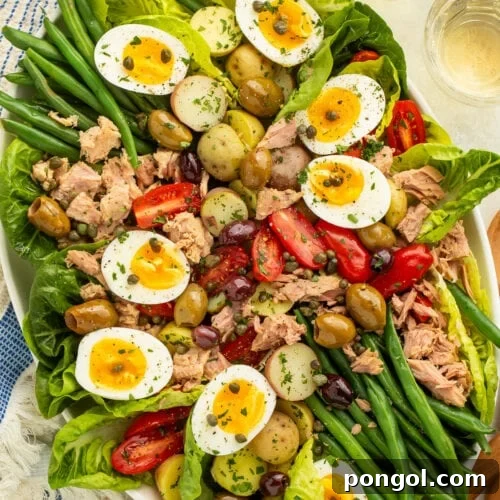 A large oval platter of Nicoise salad with potatoes, green beans, eggs, lettuce, olives, capers, tomatoes, and tuna.