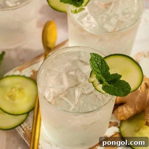 A beautifully presented Cucumber Ginger Mocktail garnished with fresh mint and cucumber, sitting on a wooden serving tray.