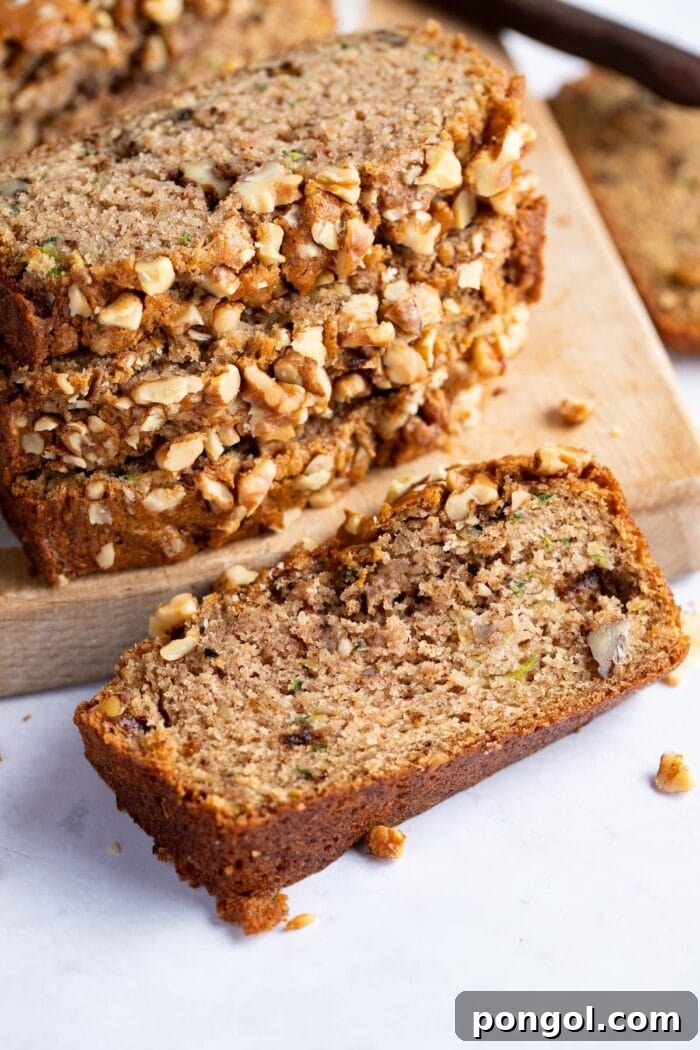 A single slice of vegan zucchini bread in front of a stack of other slices, on light surface