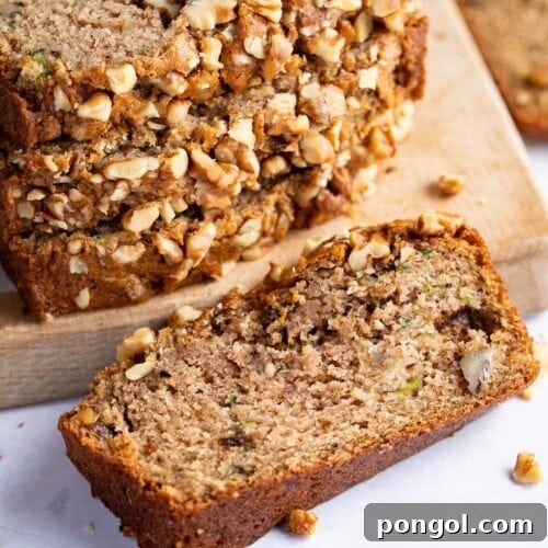 A single slice of vegan zucchini bread in front of a stack of other slices, on light surface