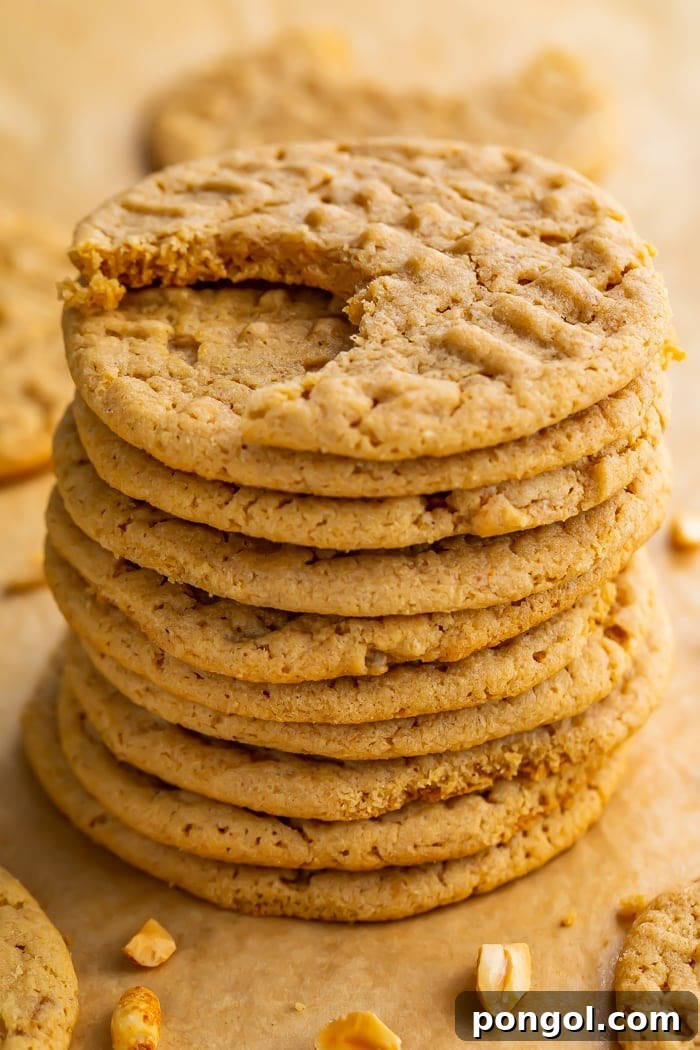 Stack of round gluten free peanut butter cookies on parchment paper. Top cookie has one bite missing, revealing the soft interior.