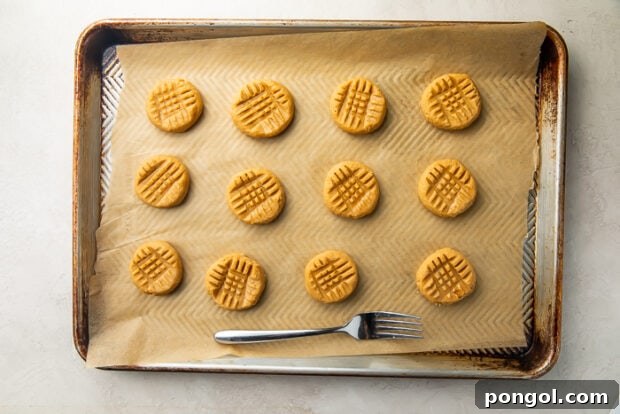 Gluten free peanut butter cookies on baking sheet lined with parchment paper next to fork used to make criss-cross pattern on top of cookies