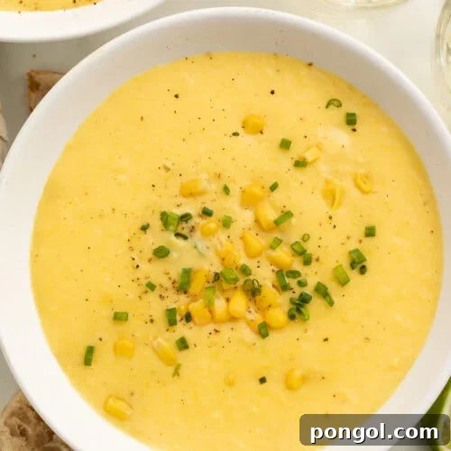 A white soup bowl holding a thick, creamy yellow corn soup topped with corn kernels and chopped green onions.