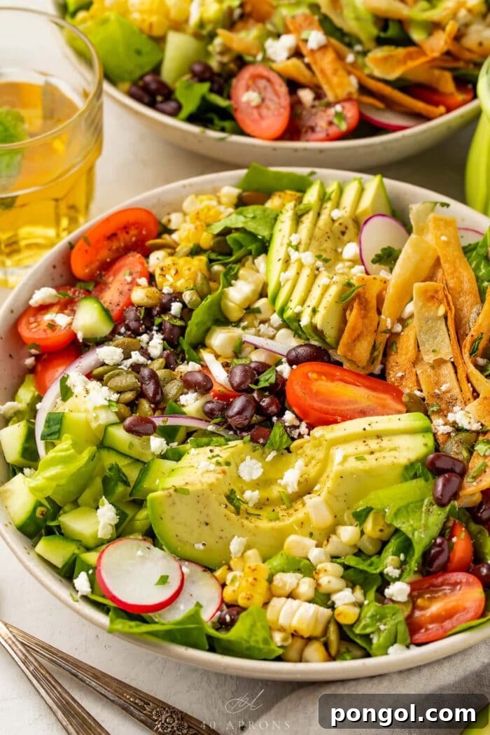 Closeup angle of Mexican salad with slices of avocado, tomatoes, tortilla strips, and onion in a white bowl.