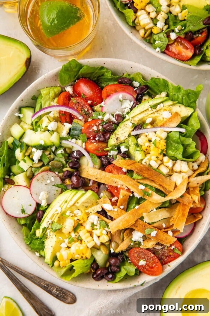 Overhead angle of Mexican salad with tortilla strips in a white bowl, next to a glass of chelada and limes.