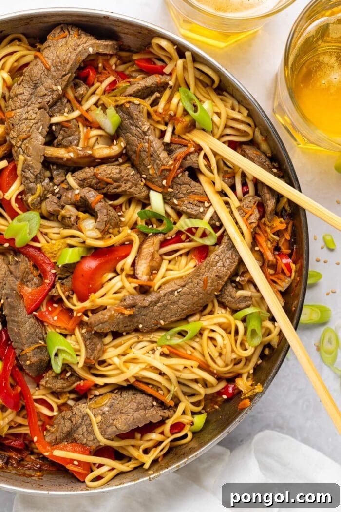 Wok-Tossed Beef Noodles 2 A large skillet filled with freshly made beef lo mein, garnished with vibrant green onions and sesame seeds, ready to be served.