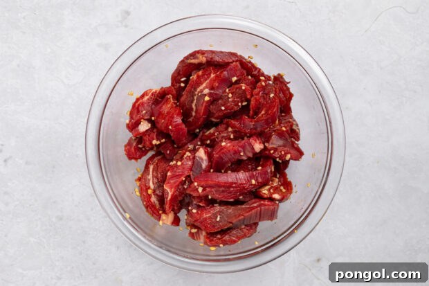 Wok-Tossed Beef Noodles 6 Sliced flank steak marinating in a bowl with soy sauce and minced garlic.