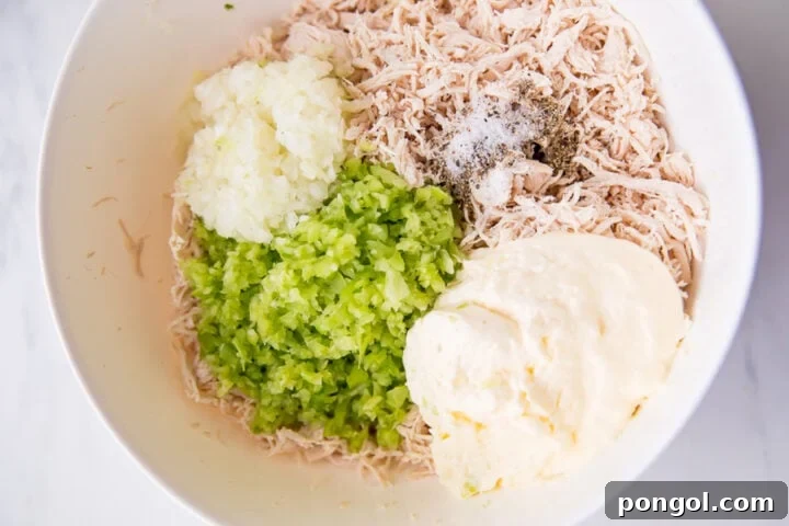 Ingredients for keto chicken salad in a large mixing bowl on a neutral background.