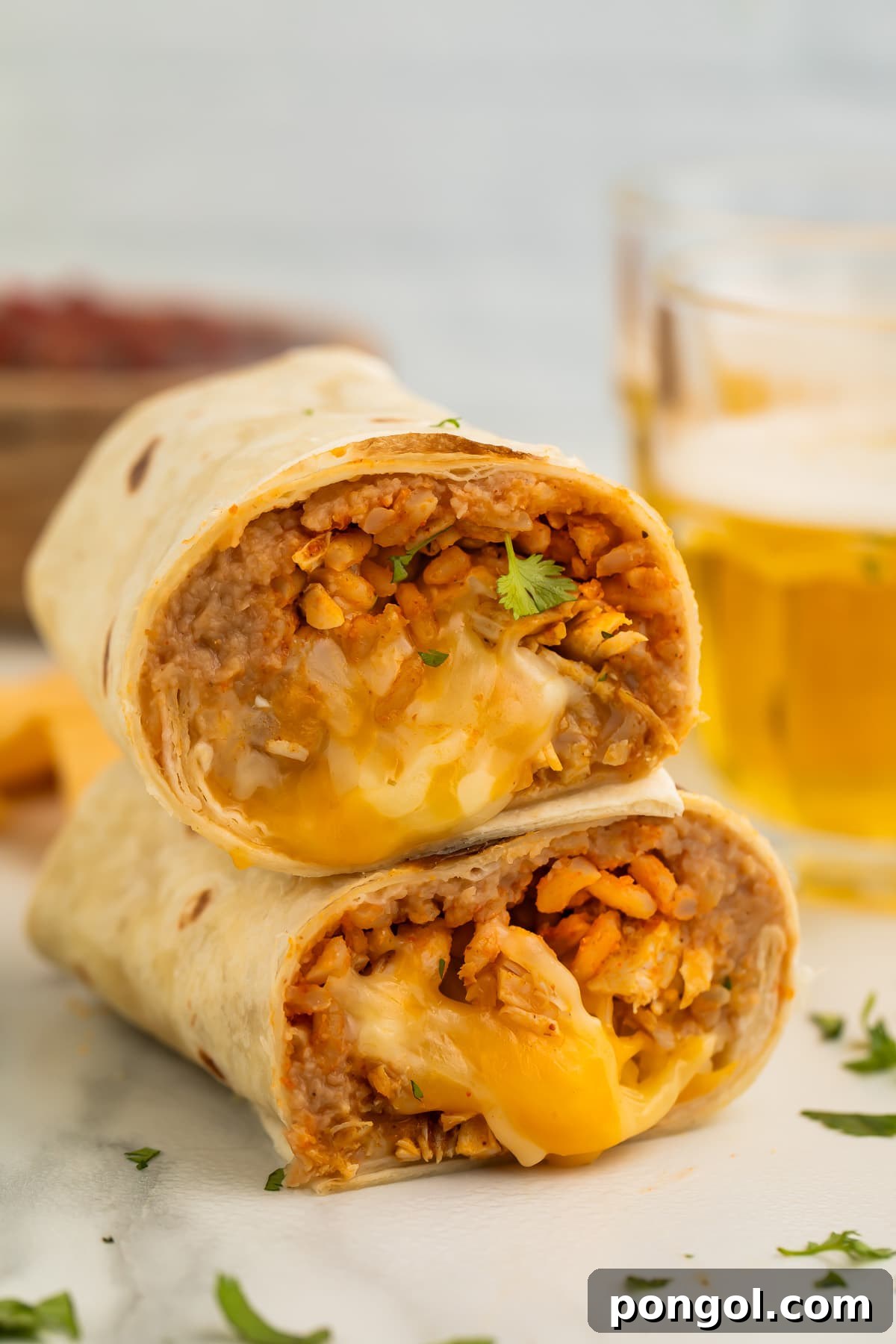 Two halves of a chicken burrito stacked on top of each other, showing a filling of chicken, rice, beans, and gooey cheese.