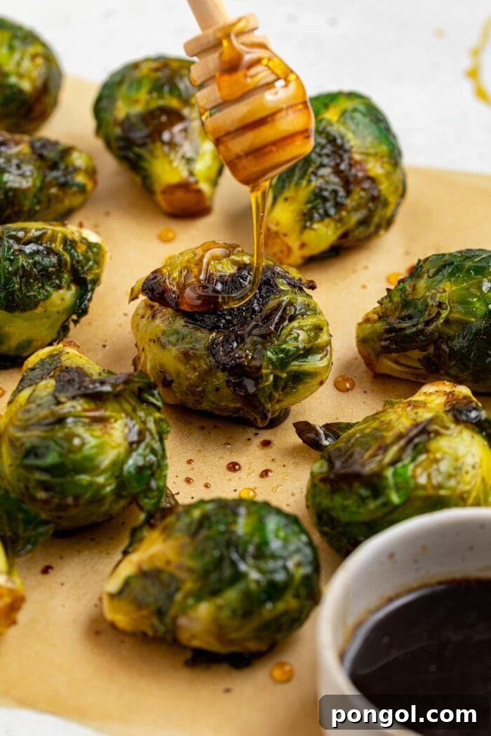 Grilled Brussels sprouts with honey being drizzled over the top, showcasing their beautiful char.