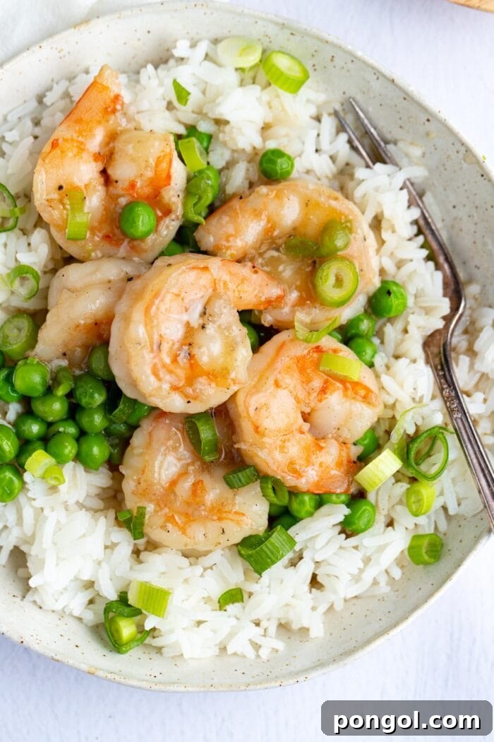 Closeup of shrimp with lobster sauce and peas on a bed of rice in a white bowl